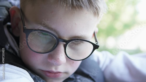 Close-up of a teenage boy sitting alone after school, wearing glasses and looking down. The scene conveys isolation, loneliness, and bullying.