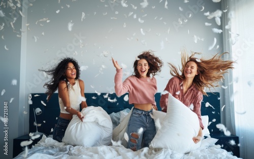 Three happy friends having a playful pillow fight in a stylish bedroom with feathers flying