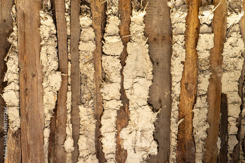 Fotografie Close-up of old adobe wall with wooden laths, clay plaster, straw fibers and cracks, showing traditional rural building material texture