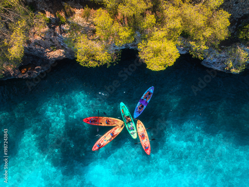 Photography Aerial drone view of colorful kayaks with people in crystal clear turquoise sea near rocky coast and green trees