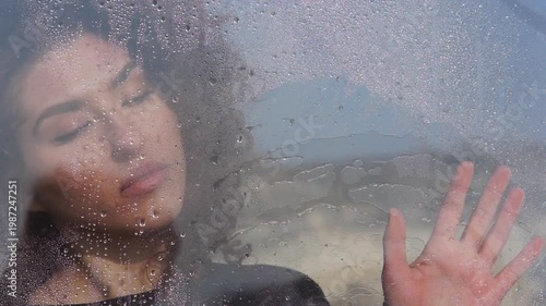 Sad woman looking through a rainy window
