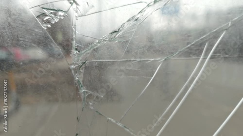 Cracked glass surface with visible fractures and reflections, showcasing a blurred urban street scene with vehicles and signs in the background