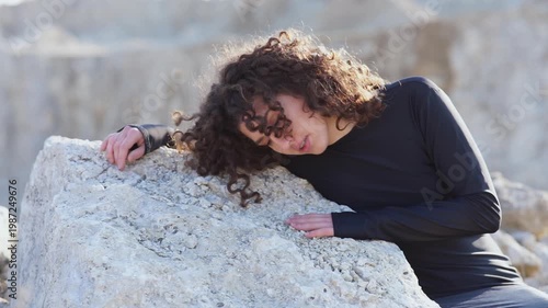Tired woman with curly hair resting on a stone in a quarry