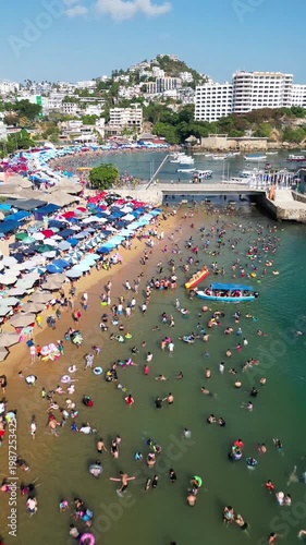 Vibrant Caleta and Caletilla beaches in Acapulco, Mexico, captured by low altitude drone on a sunny day. Many people swimming, sunbathing, and enjoying the tropical paradise.