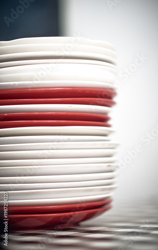 A stack of red and white ceramic plates in a cafe setting, showing repetition, texture and minimal composition, representing food service, hospitality and kitchen environment