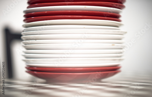 A stack of red and white ceramic plates in a cafe setting, showing repetition, texture and minimal composition, representing food service, hospitality and kitchen environment