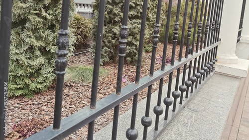Black wrought iron fence with decorative elements and greenery in the background, showcasing a continuous view of the fence from different angles in an outdoor setting