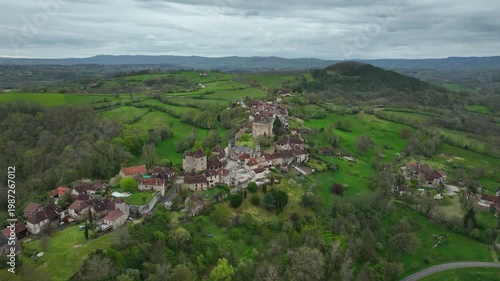 Aerial view of Curemonte France with Saint Hilaire castle and historic village perched on a hill surrounded by lush green rolling countryside under cloudy sky