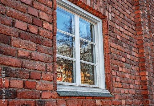 A white wooden window frame with glass panes is set into a red brick wall of an old building.