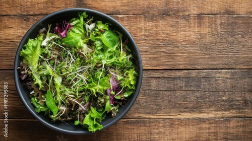 A fresh salad bowl filled with mixed greens and herbs sits on a rustic wooden table, showcasing vibrant colors and textures.