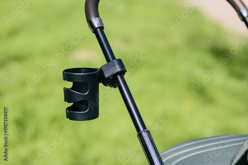 Close-up of stroller handle with black cup holder attached, isolated against blurred green park background, minimal modern parenting accessory and outdoor lifestyle concept for product advertising
