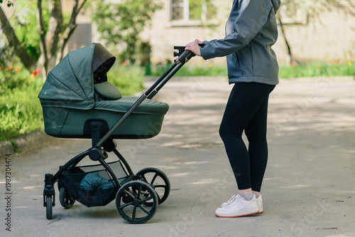 Woman walking with modern baby stroller on sunny park path, close side view with green background, active parenting lifestyle and outdoor прогулка concept for family and childcare advertising