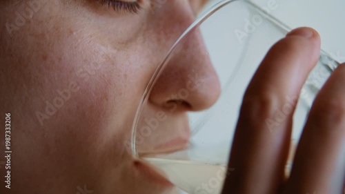 Close-up of a young woman feeling unwell holds a glass of effervescent vitamin C medicine and drinks it slowly while looking out the window