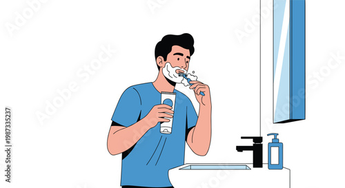 Young man in a blue t-shirt standing in front of a bathroom mirror and shaving his face with a razor and foam.