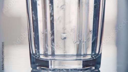 Crystal-clear water flows into a transparent glass, with bubbles rising to the top. The soft, natural morning light highlights the simplicity and refreshment of a daily home ritual.