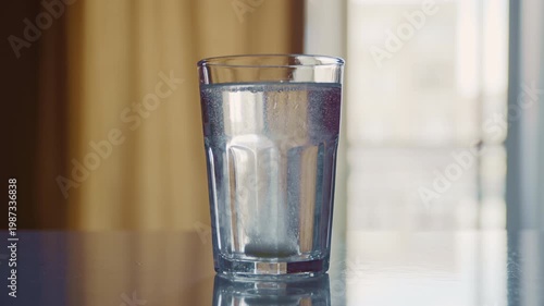 A healing tablet placed in clear water rapidly dissolves, producing carbonation and small particles swirling inside the glass. 