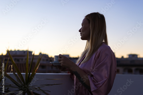 Фотография Woman enjoying morning coffee ritual on a city rooftop, watching the sunrise and