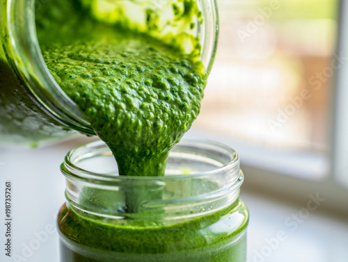 Extreme close-up of green kale and spinach smoothie pouring into mason jar with water droplets, macro food photography in sunlit kitchen