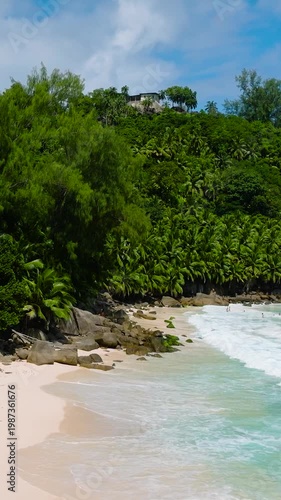 Large rocks and dense tropical greenery extend to the edge of the sandy beach meeting turquoise waters. Anse Intendance. Seychelles, Mahe.