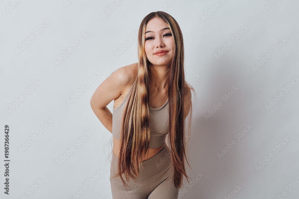 Naklejka premium Young woman with long braided hair posing and smiling in casual beige outfit against white background. Beautiful female model with relaxed posture and confident expression.