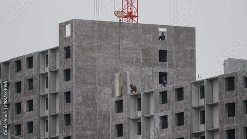 Building facade assembly. Construction crew carefully places precast sections on multilevel facade using safety harnesses and mobile crane