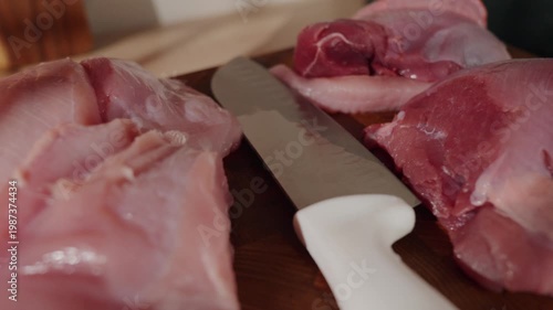 Closeup of trimming process for turkey in small kitchen. Chef expertly slices pink pork ready for seasoning on wooden chopping board