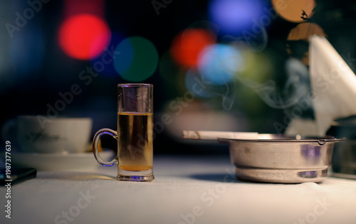 Alcohol shot and smoking cigarette in ashtray stand on a table in a bar at night