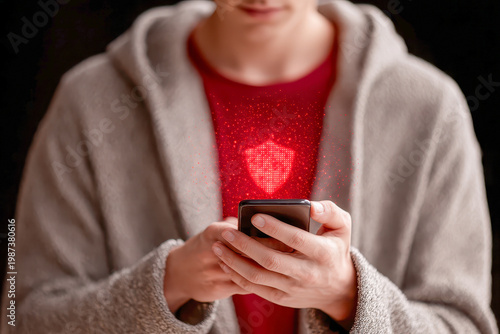 Young man holding smartphone with red glowing digital shield hologram. Mobile cybersecurity concept, data protection, and virus threat warning.