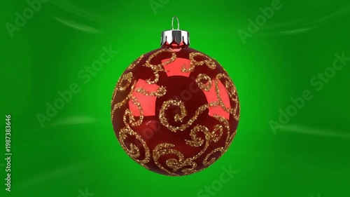 Red Christmas ornament with golden swirls hanging against a smooth green backdrop, rotating slowly
