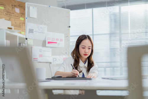 Bilde på lerret A focused young Asian female entrepreneur using a stylus pen to draw on a digital tablet at her office desk