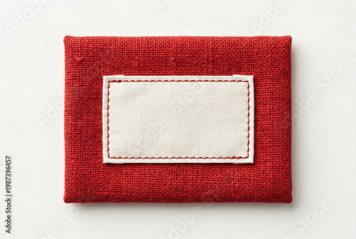 Blank white rectangular label sewn onto red fabric, realistic mockup with copy space for branding and design elements.