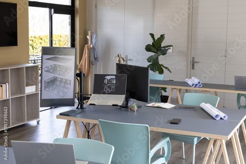 Central workstation table showing architectural plans on laptop and vertical monitor at studio