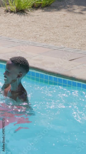 Vertical video: Splashing teen wearing red swim trunks cooling off in sun at home pool, copy space