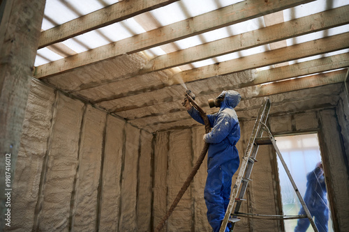 Foto Installer covering overhead framing with spray foam insulation in house under construction