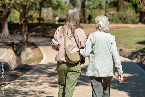 An 85 year old grandmother and her daughter enjoy a walk together in a sunny park