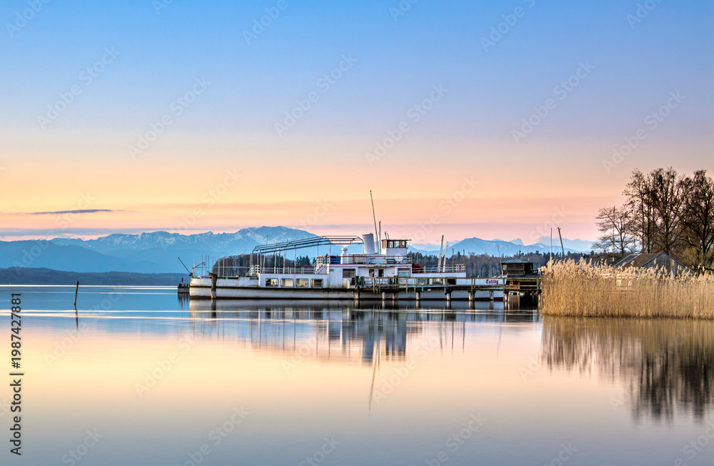 Obraz premium Altes stillgelegtes Ausflugsschiff an einem Holzsteg spiegelt sich im klaren Wasser im Morgenlicht am Starnberger See, Tutzing, Bayern, Deutschland Europa