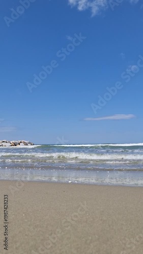 Minimalistic coastal video landscape featuring a sandy beach, blue sea, gentle waves, and a clear sky. Summer travel backdrop with a calm ocean horizon and natural text space.
