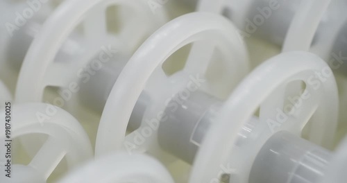 An industrial conveyor is in operation, white plastic rollers are rotating. Static handheld shot of production, sorting, or transportation line, real time speed, artificial lighting.