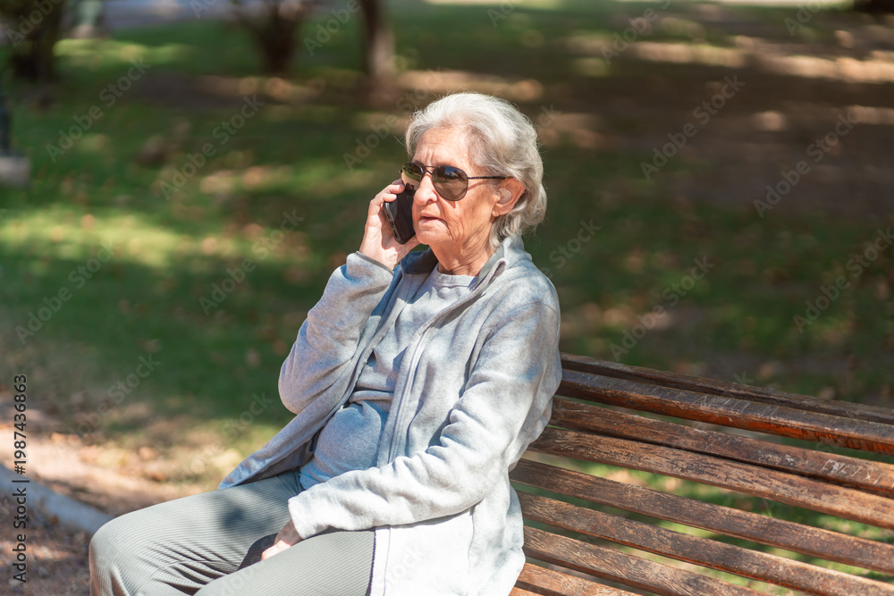 Fototapeta premium An 85-year-old grandmother enjoys a phone call while sitting on a park bench