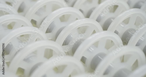 An industrial conveyor is in operation, white plastic rollers are rotating. Static handheld shot of production, sorting, or transportation line, real time speed, artificial lighting.