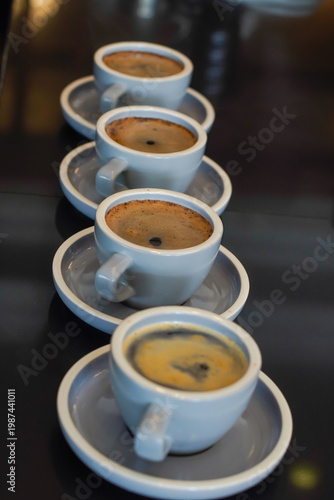 Close up of espresso cups in a row with shallow depth of field, showing crema texture. Ideal for coffee culture, café lifestyle, barista, and specialty coffee concepts.