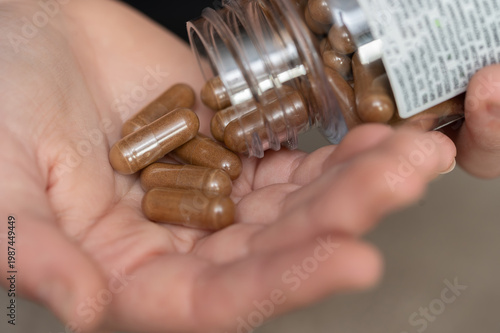 Person pouring brown herbal capsules from a bottle into their hand. Close-up of hands holding natural medicine pills or supplements.