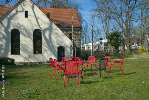 Vibrant red chairs arranged in a circle on a green lawn in front of the historic parish house in Berlin Rudow, Germany