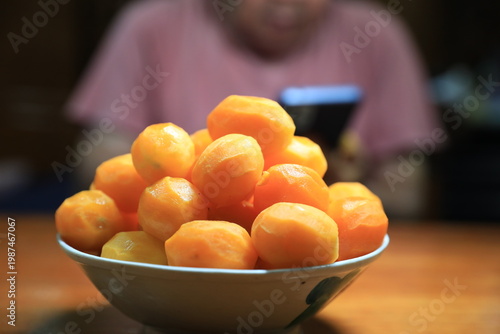 Fresh peeled Thai marian plums, also known as mayongchid or maprang, arranged in a white bowl on a wooden table. 