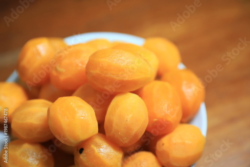 Fresh peeled Thai marian plums, also known as mayongchid or maprang, arranged in a white bowl on a wooden table. 