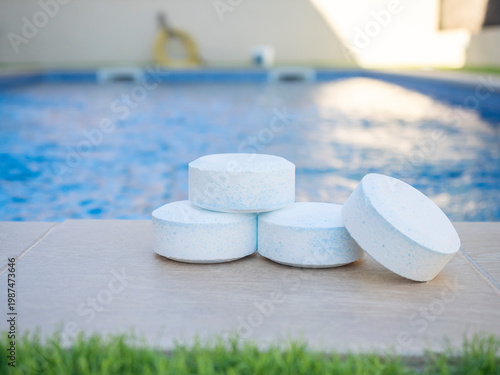 Photos Close-up of chlorine tablets placed near a swimming pool, used for water sanitat