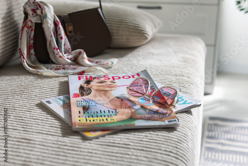 Lifestyle magazines and glasses on sofa indoors, closeup