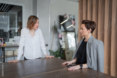 Fényképezés Two women in business clothing sharing ideas and discussing at worktable in modern well-lit office