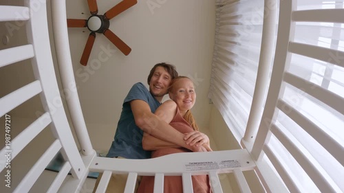 Smiling mother and father hugging and looking at their newborn in a crib, filmed from baby point of view. Tender family moment full of love and care. Parenthood, bonding and newborn care concept