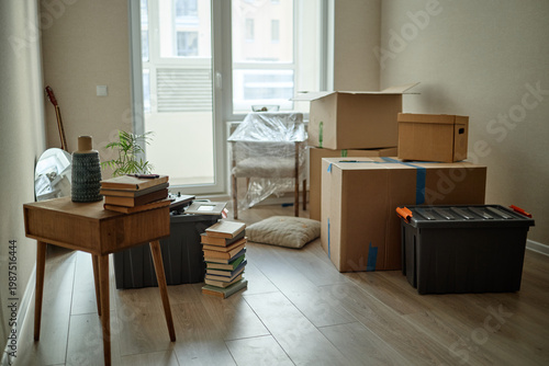 Tableau sur toile Wide shot of packed moving boxes, storage bins, books, chair, and decor filling empty apartment, suggesting relocation and home setup